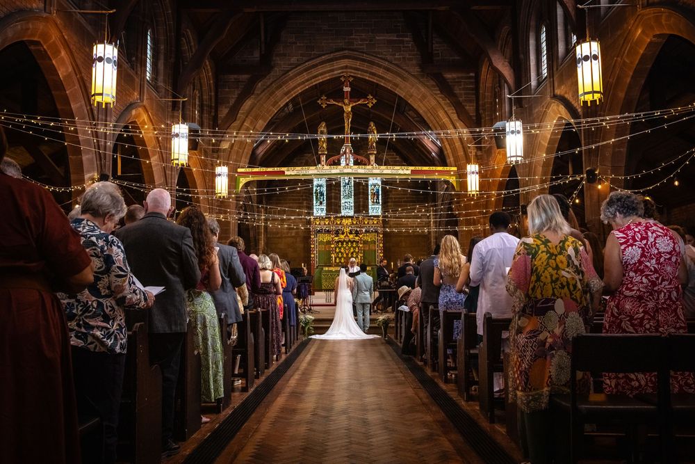 Wide angle view of bride at altar in stunning historic church adorned with fairy lights.