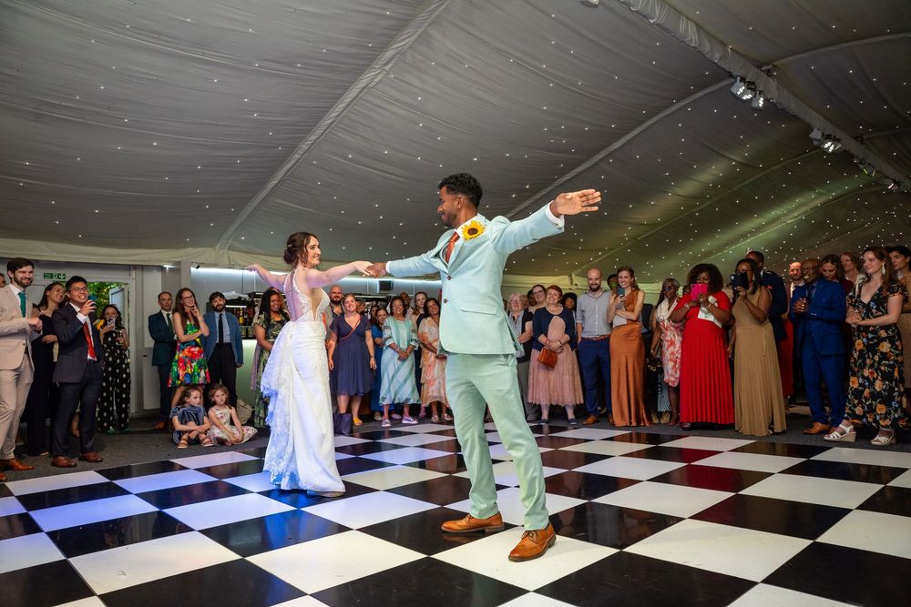 Bride and groom perform their first dance on a black and white checkered dance floor.