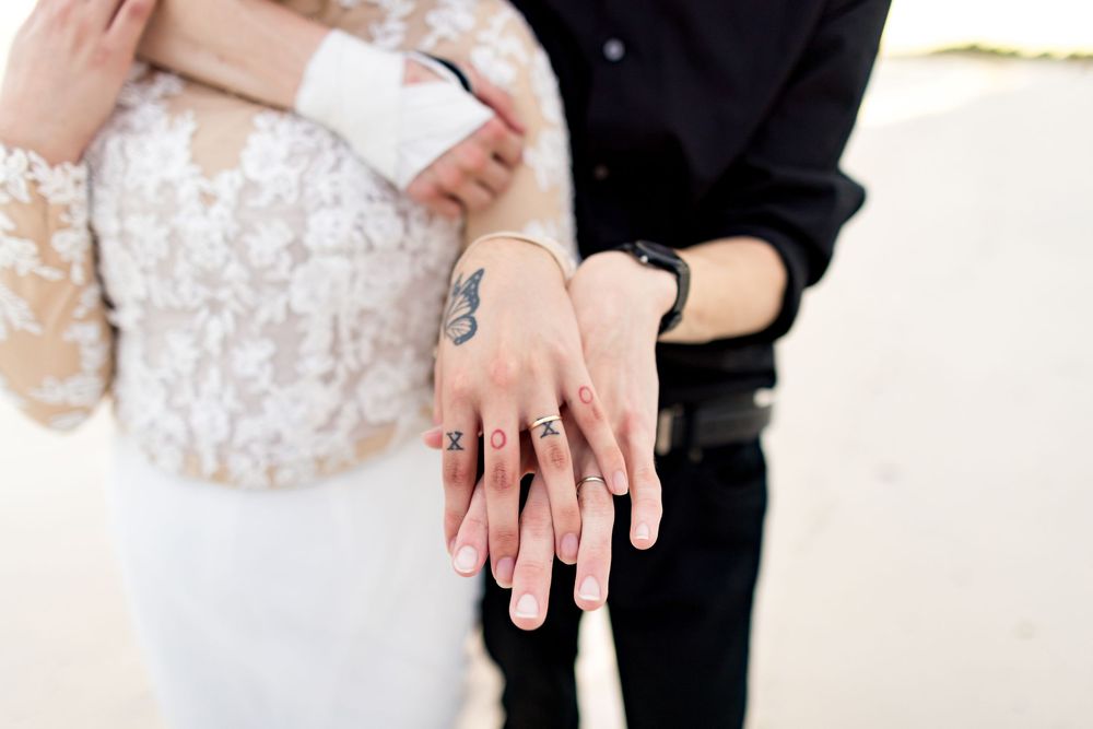 Close-up shot of hands holding each other in a romantic gesture, showcasing wedding rings and manicured nails.