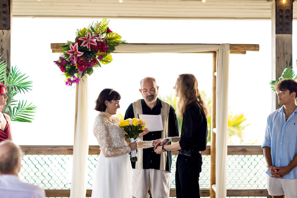 A group of people gather at an indoor event space with wooden beams and floral decorations.