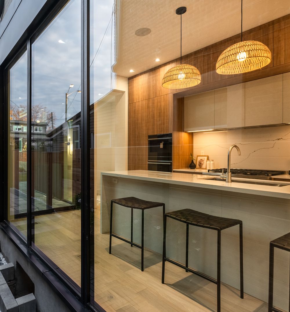 Modern kitchen interior with woven pendant lights, wooden cabinets, and a white breakfast bar with black bar stools.