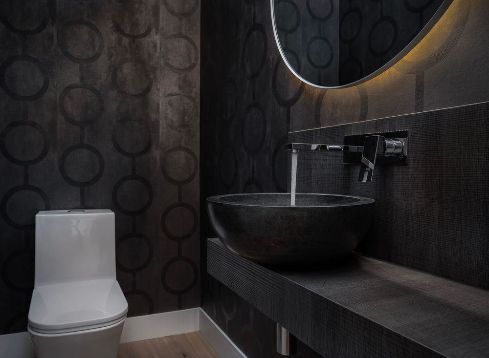 Modern dark bathroom interior with black patterned walls, floating vanity, and contemporary white fixtures.