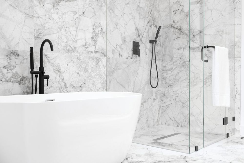 Modern luxury bathroom featuring a freestanding white bathtub and black fixtures against a marble wall with glass shower enclosure.