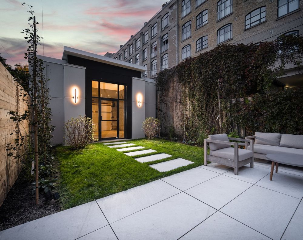 Modern residential building exterior with illuminated walkway and concrete steps leading to entrance at dusk.