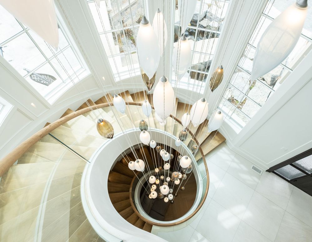 Looking down a curved spiral staircase with white walls and wooden steps illuminated by hanging glass pendant lights.