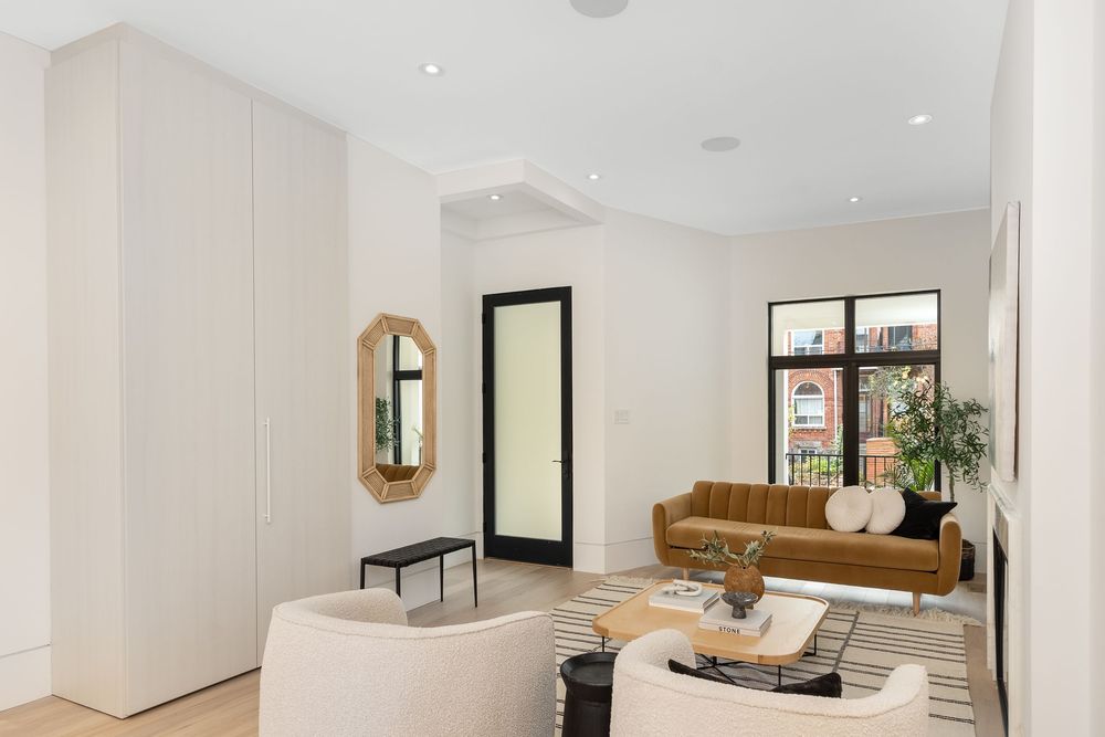 Modern minimalist living room with white walls, brown leather sofa, and large windows letting in natural light.
