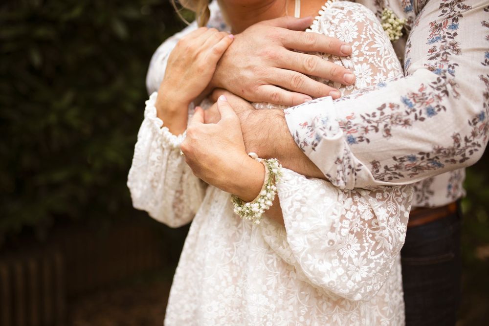A person wearing a white lace dress with long sleeves holds their hands together in front of their body.