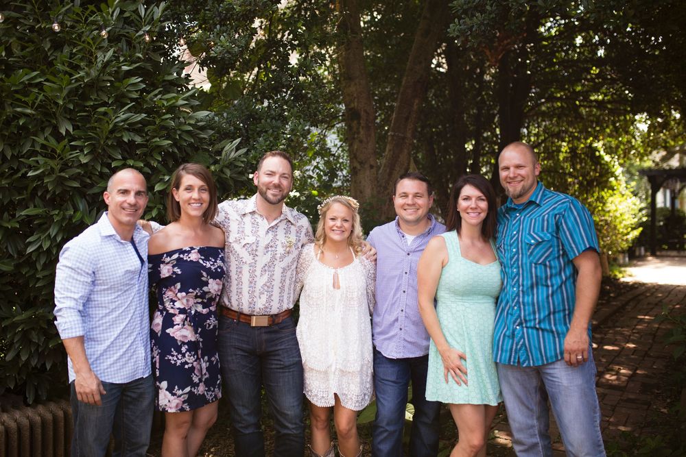 A group of people standing together outdoors in casual attire for a family photo in a wooded setting.
