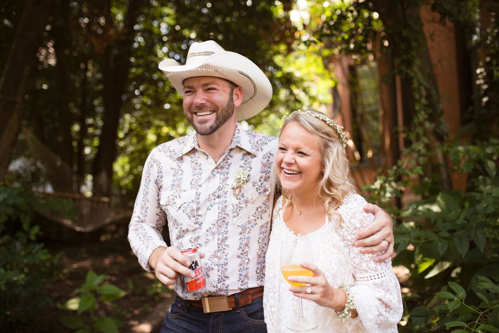 A couple laughs together while enjoying wine in an outdoor garden setting during a sunny afternoon.