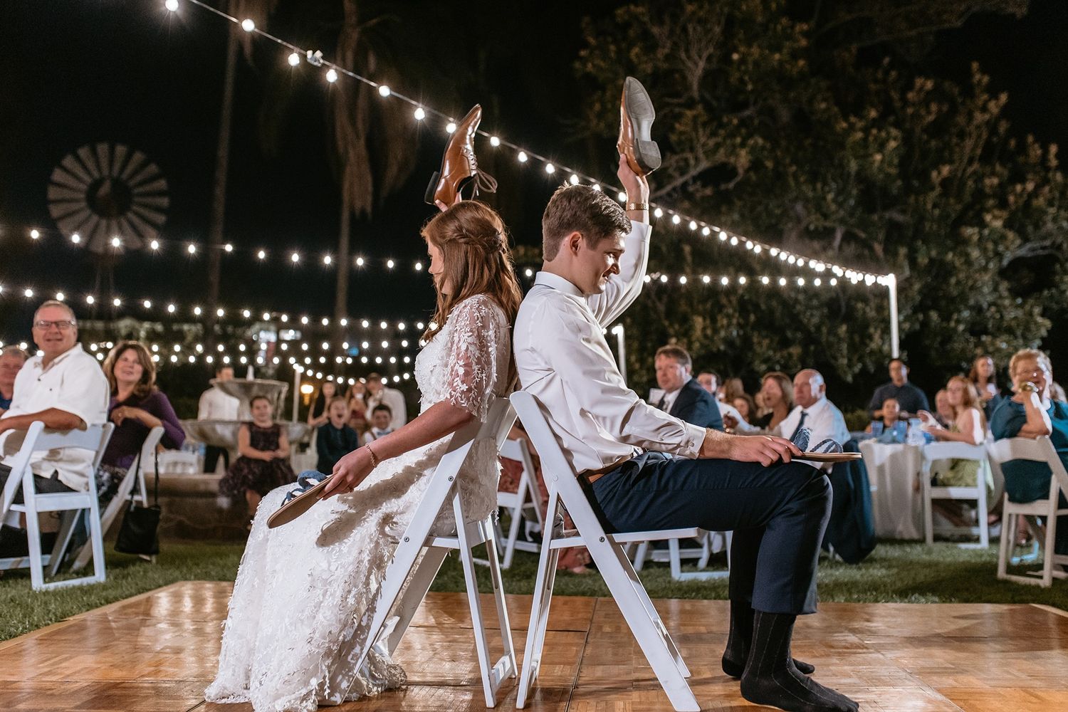 Bride and groom playing the shoe game at outdoor wedding reception with string lights at night at Rancho Buena Vista Adobe.