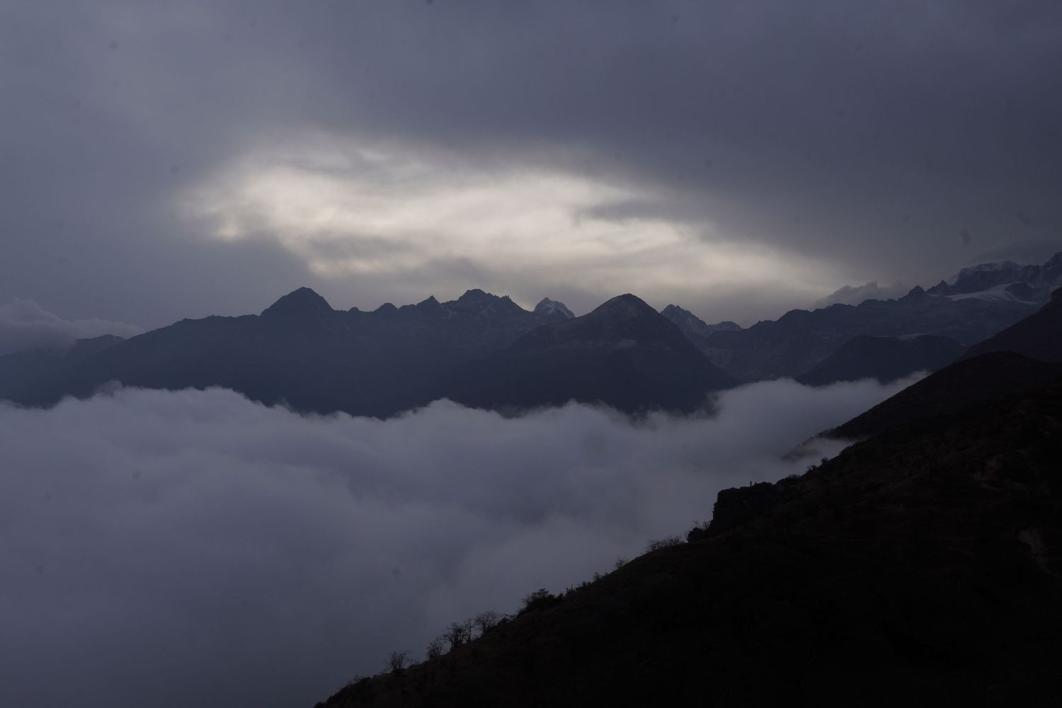 Atmospheric view of jagged Himalayan peaks emerging above a thick bed of clouds at sunrise.