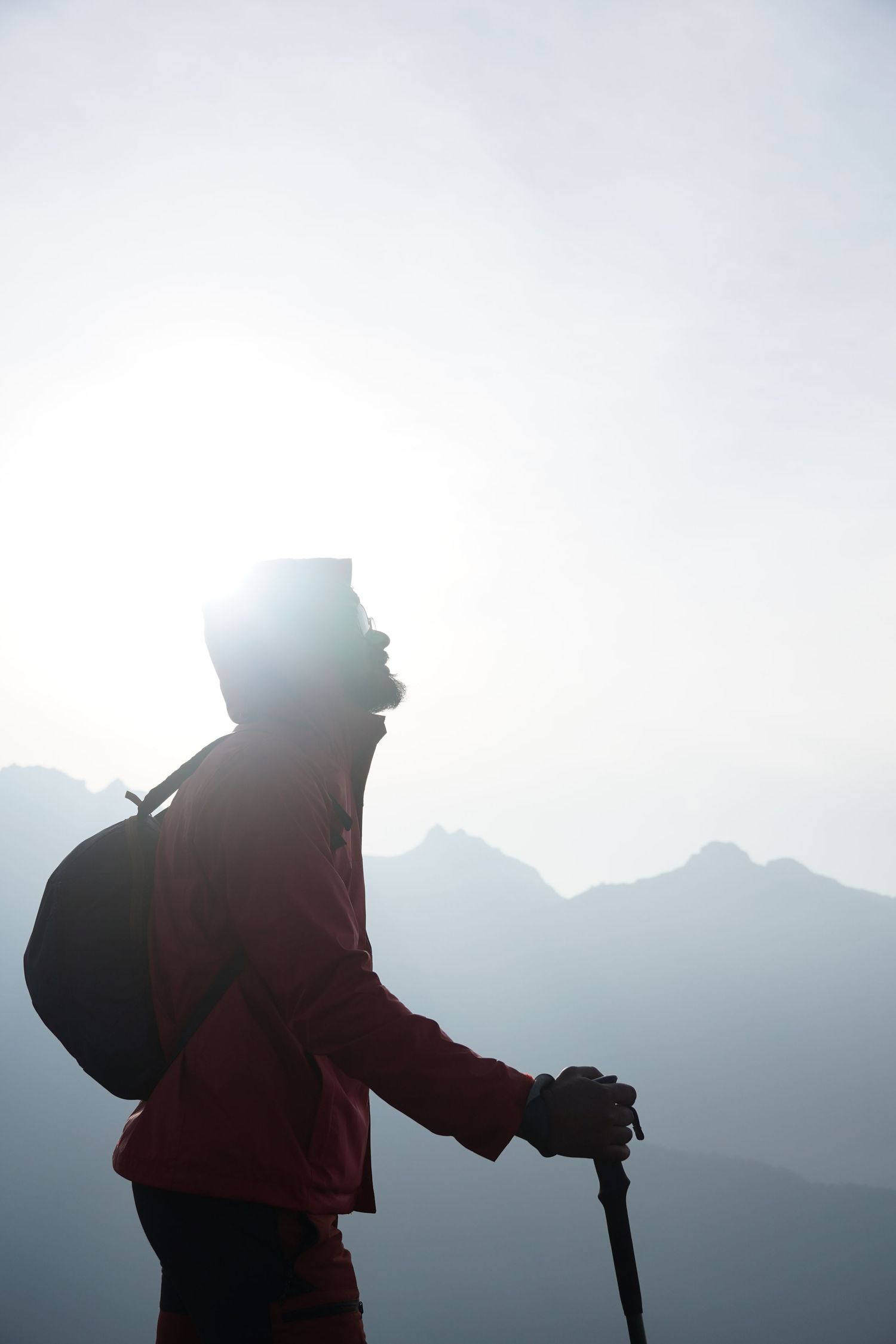 High-contrast silhouette of a trekker with trekking poles against a brilliant sunburst, symbolizing the end of a long journey.