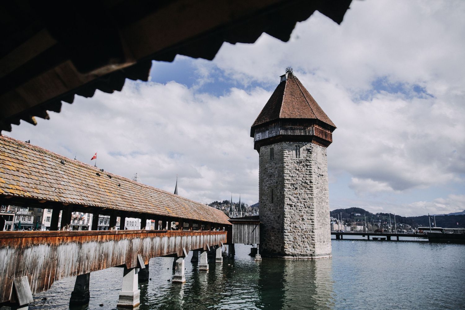 Historic Chapel Bridge and Water Tower in Lucerne, Switzerland, spanning the Reuss River under a cloudy sky.