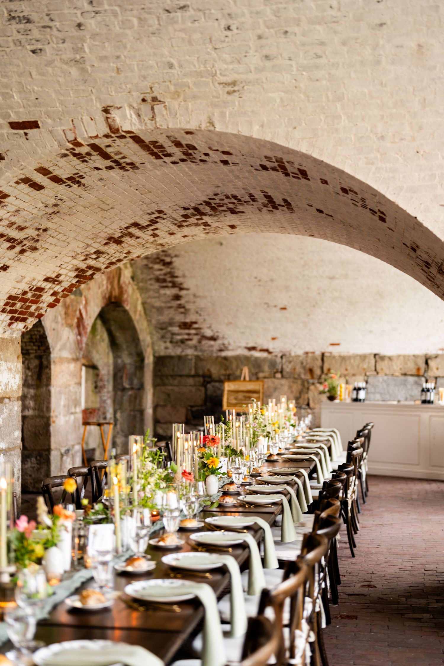 Elegant wedding reception table setting under brick arch with floral centerpieces.