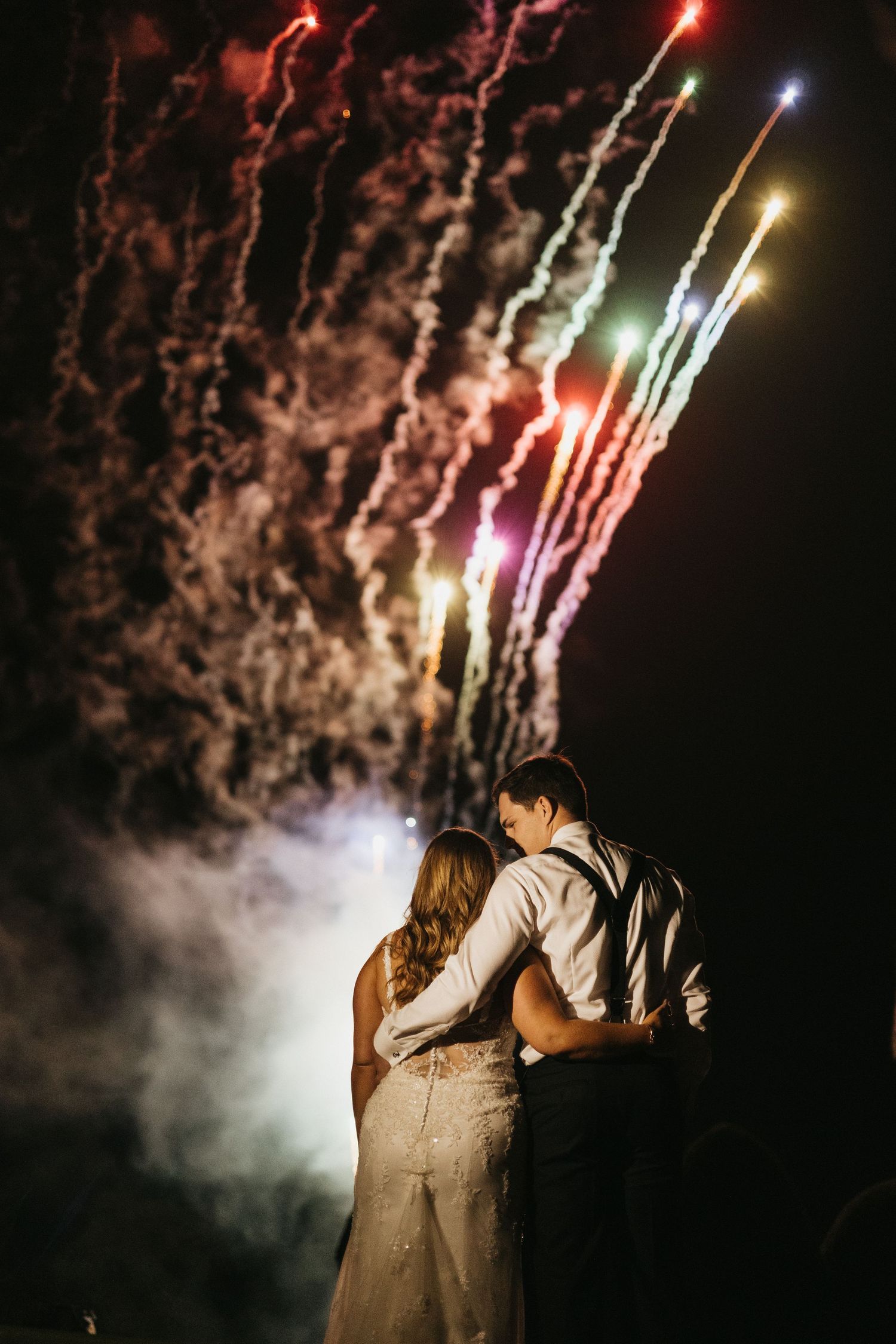 A romantic couple embraces while watching colorful fireworks light up the night sky during a celebration.