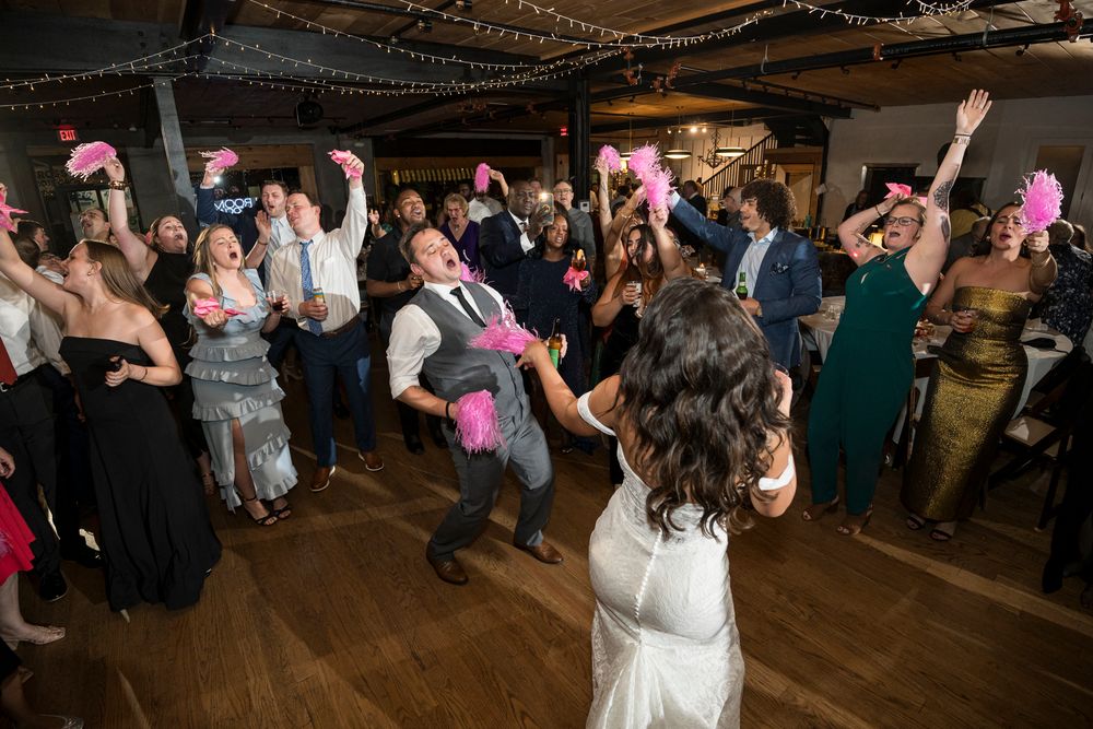 Wedding guests dance and celebrate on a wooden dance floor during a lively reception party.