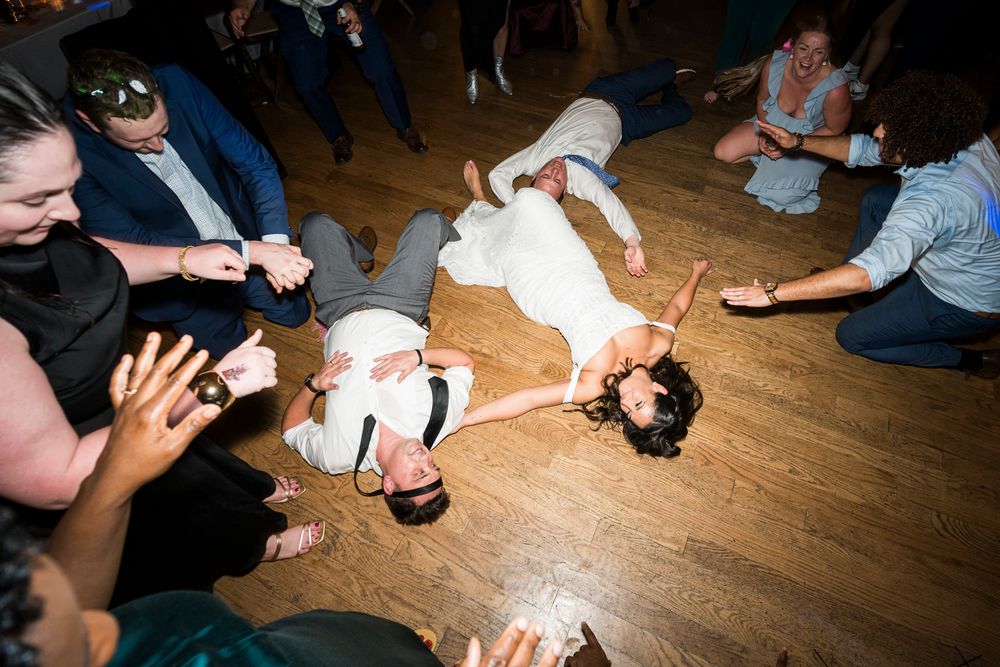 Energetic dancers performing breakdance moves on a wooden floor surrounded by an enthusiastic crowd at a party.