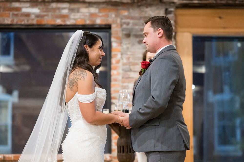 A couple shares a tender moment during their wedding ceremony in front of a rustic brick wall backdrop.