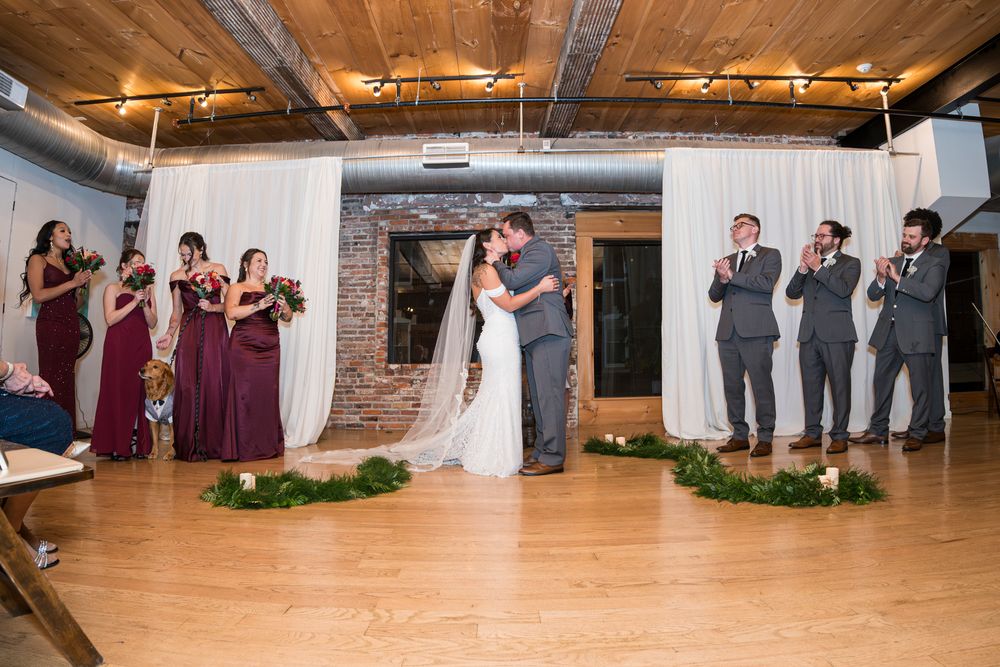 Wedding party dancing and celebrating in a rustic indoor venue with exposed brick walls and wooden floors.