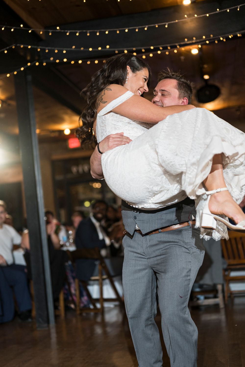 A couple shares a romantic dance moment at a wedding reception under twinkling string lights.