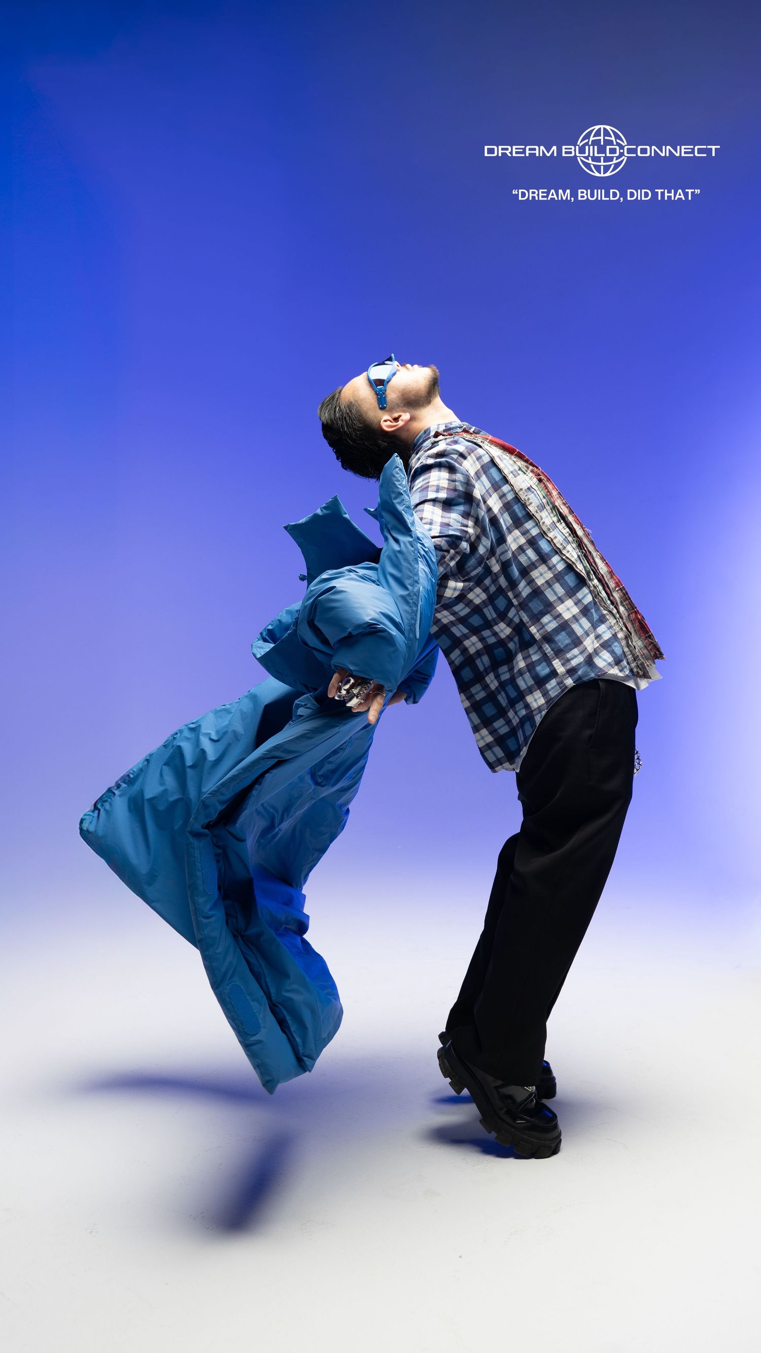 Two models in dynamic pose wearing blue puffer coat and plaid jacket against blue background.