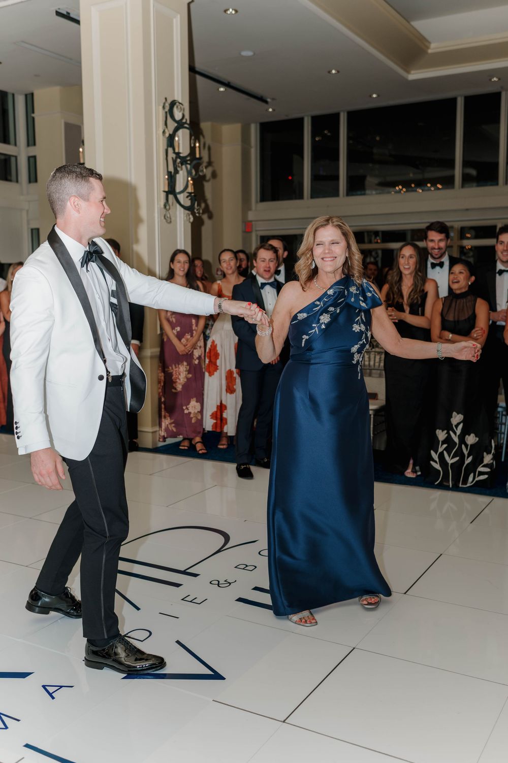 Wedding guests dance together on a white dance floor during a formal reception celebration.