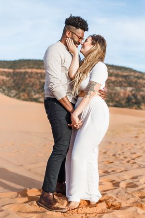 An intimate couple shares a tender moment while sitting on vibrant desert sand dunes.