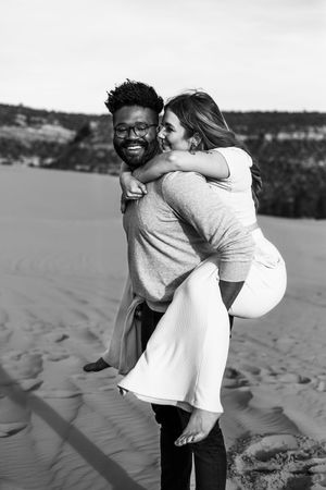 A playful black and white sequence of a couple embracing and laughing on sand dunes.