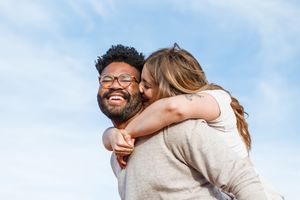 Happy couple embracing and laughing together outdoors against a bright blue sky.