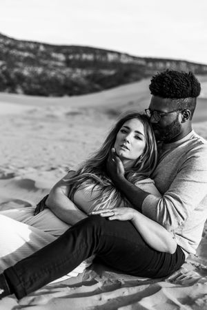 Black and white portrait of a couple embracing on sandy dunes during sunset.
