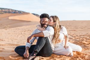 A couple shares romantic moments while lying on desert sand dunes.