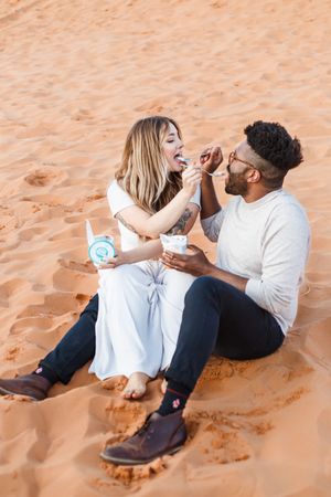 A couple lounges together on orange sand dunes sharing tender moments in the desert sunlight.