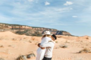 Person in white top and jeans exploring scenic desert landscape with red rock formations under blue sky.