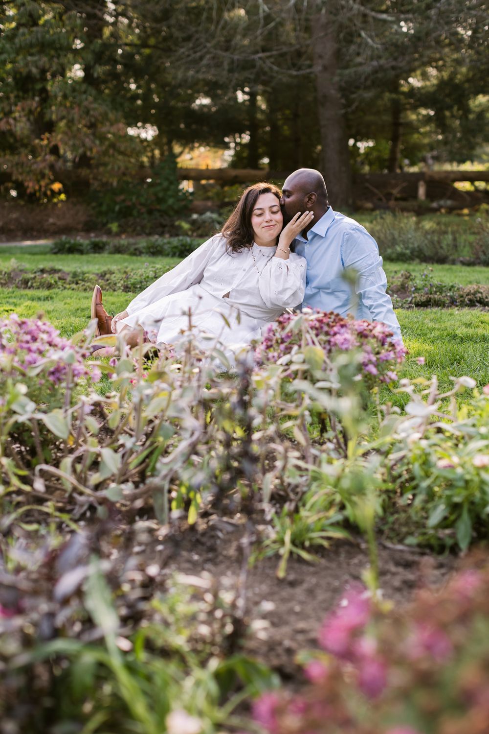 Man in blue shirt kisses woman on cheek sitting by flowers at Garden at Elm Bank in Wellesley for couple photos Seacoast couple photographer
