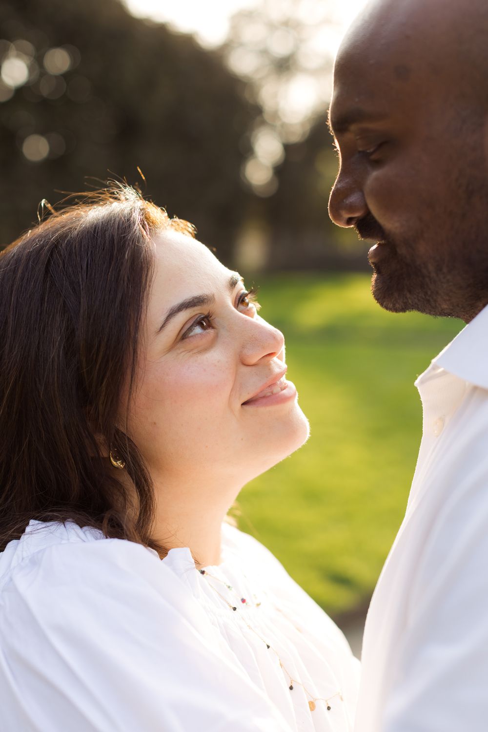 Man and woman wearing white shirts gaze at each other with sunlight on their faces for couple photos at Garden at Elm Bank in Wellesley.