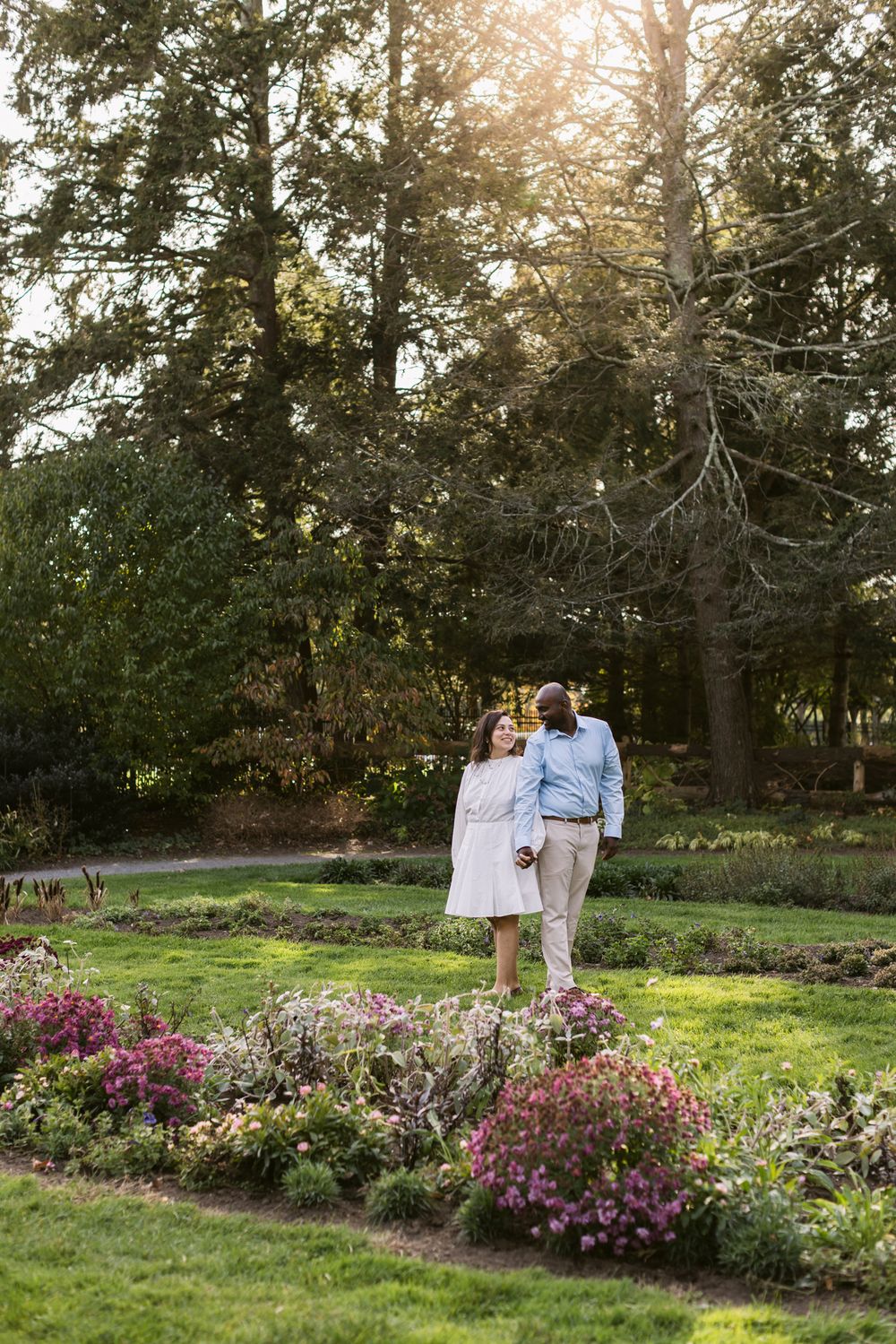 Man and woman stand pose at Garden at Elm Bank with sun flare through trees for couple photos. Laconia Alton Bay Rye couple photographer