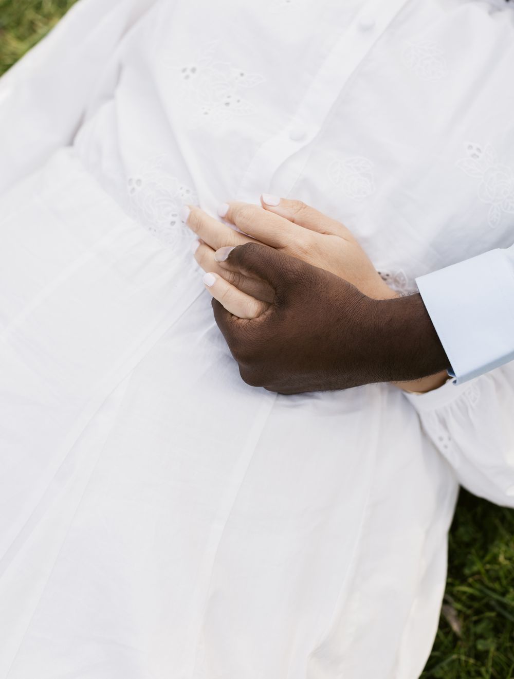 A man embraces his girlfriend's hand, holding it over her white dress for couple photos. Seacoast Hampton New Hampshire couple photographer