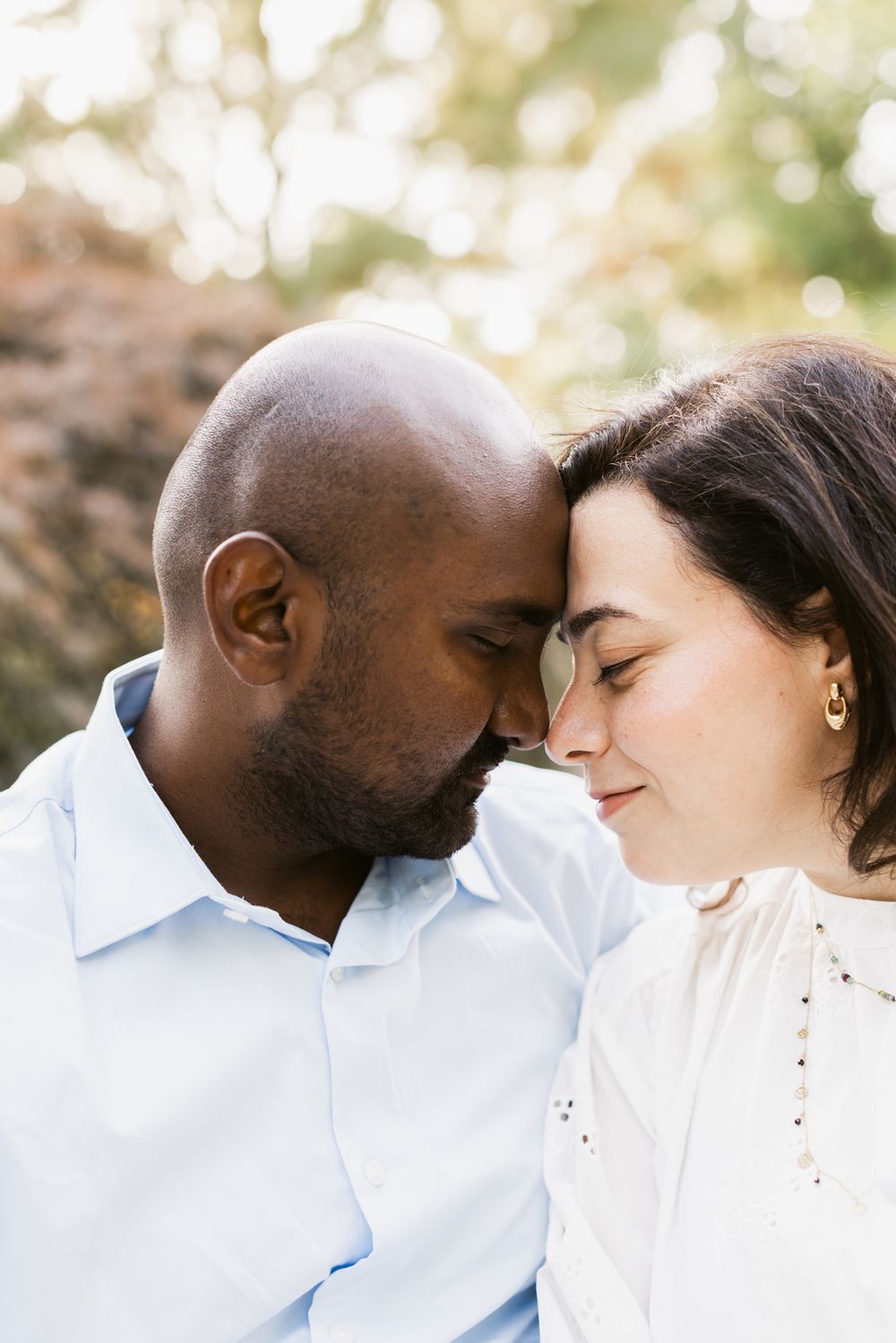 A man and woman close their eyes and put their foreheads together at Garden at Elm Bank with autumn lit bushes in background