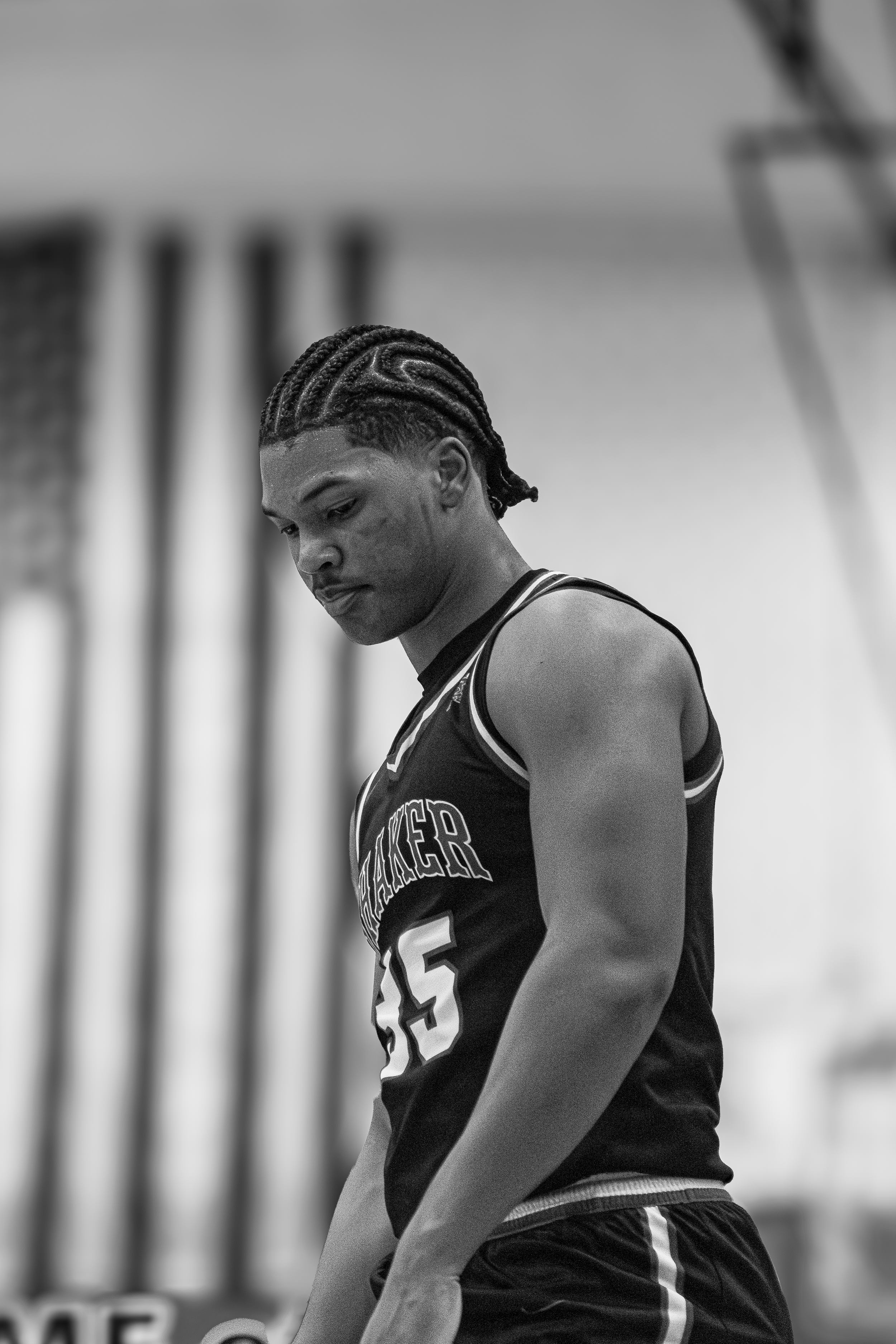 Gritty black and white portrait of a basketball player looking down with focus in a gym.