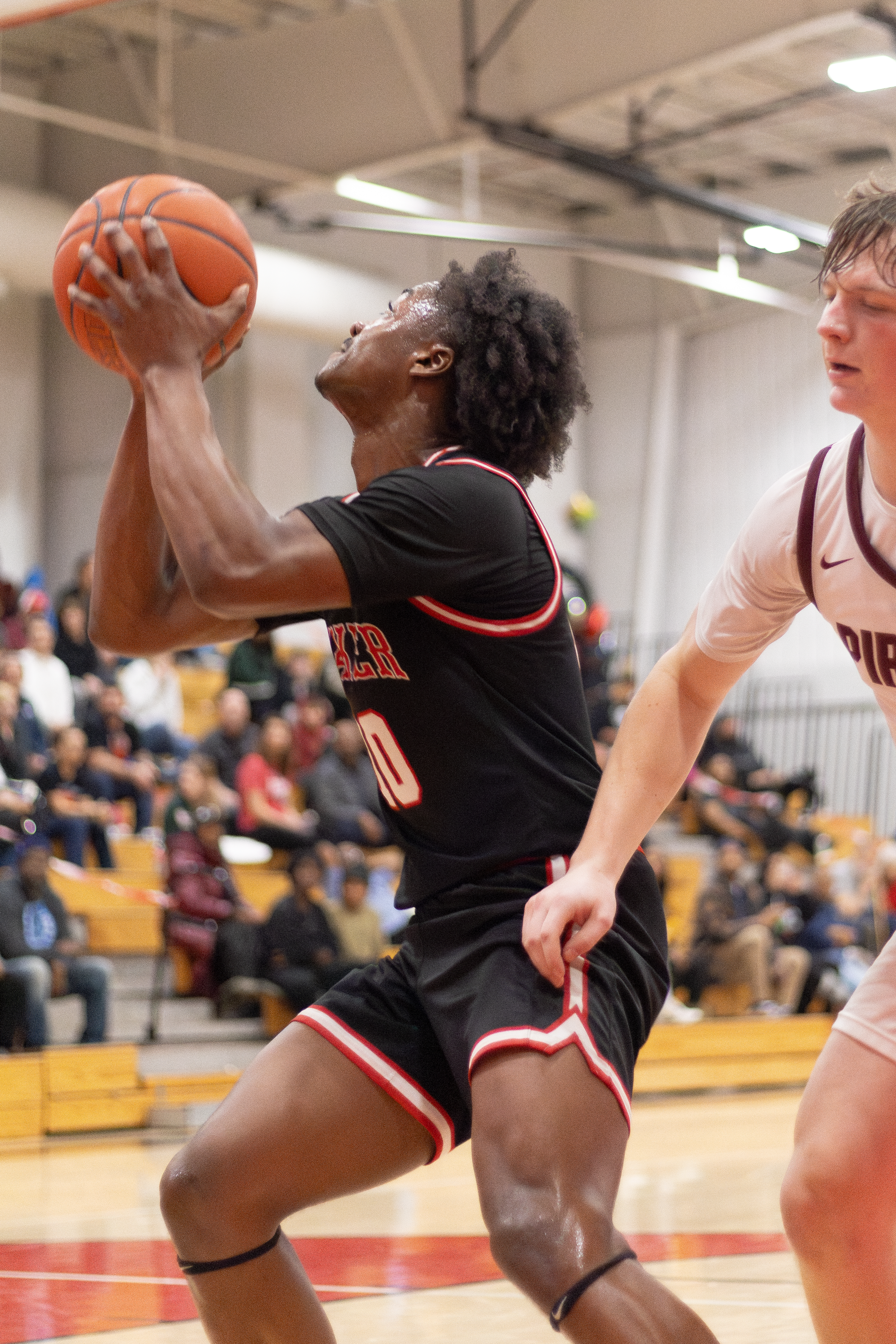 Basketball player in a black jersey jumping for a layup during an indoor game.