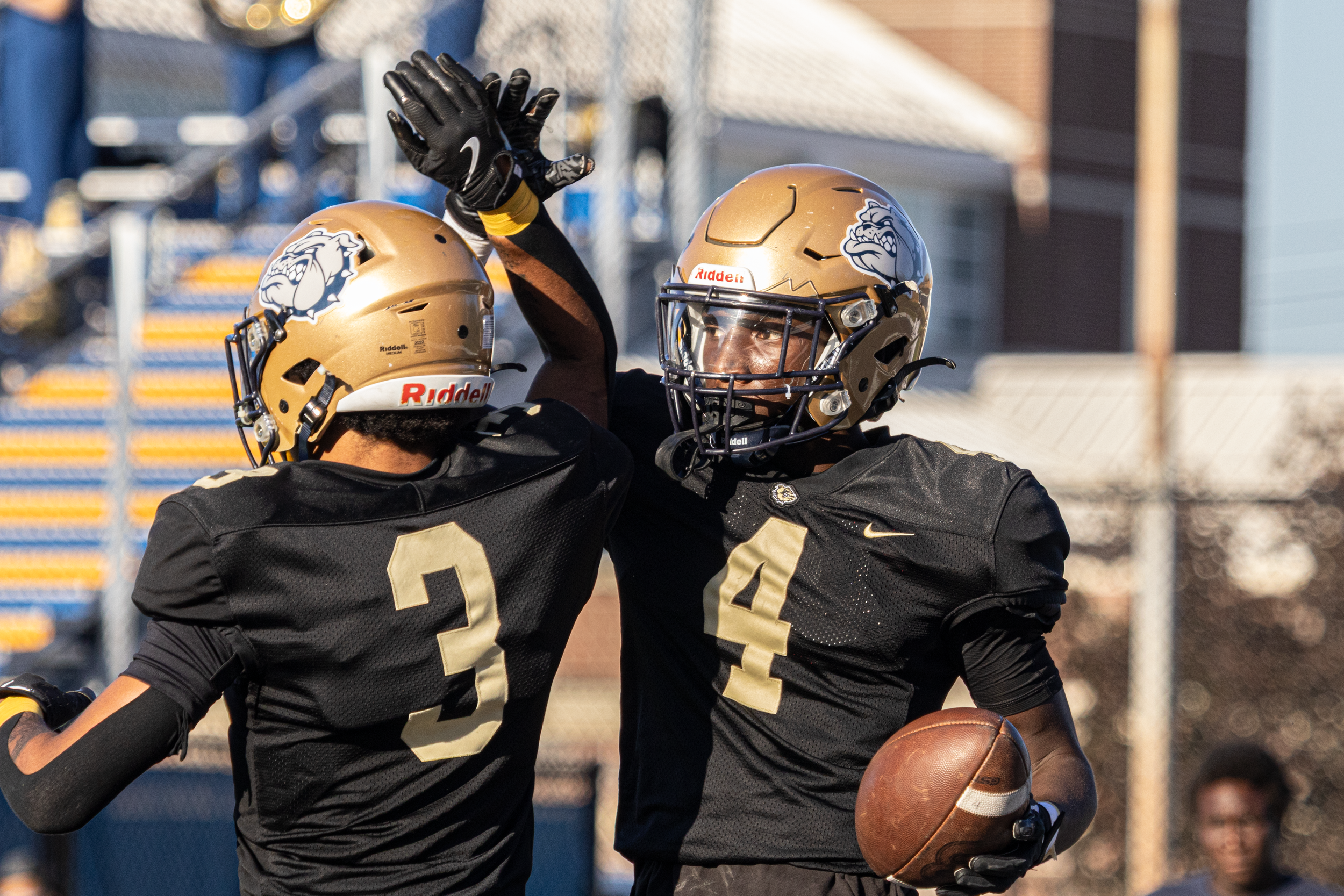 Two football players in gold Bulldog helmets celebrating a play with a high-five on the field.