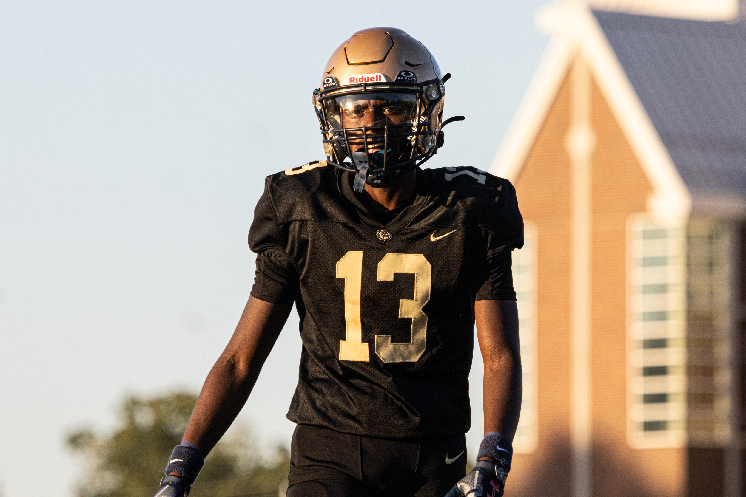 Close-up of a football player in a black and gold jersey and Riddell helmet looking at the camera.