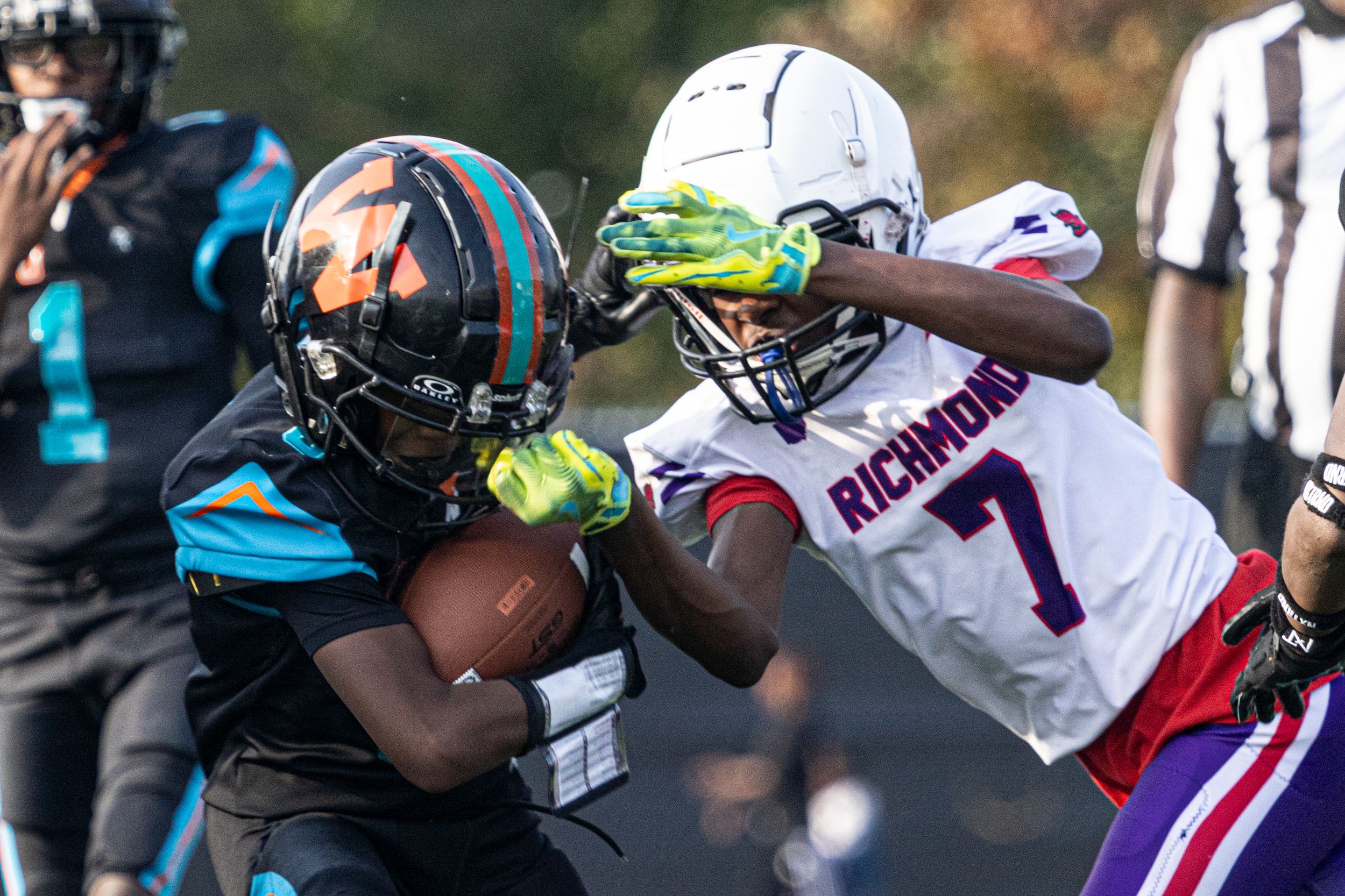 Football player in a white Richmond jersey tackling an opponent in a black and teal helmet.