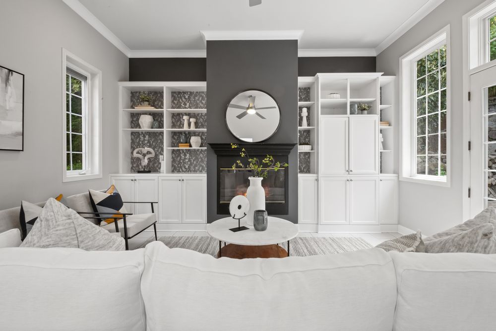 Elegant living room with white sectional sofa, gray fireplace wall, built-in shelves, and large windows flooding natural light.