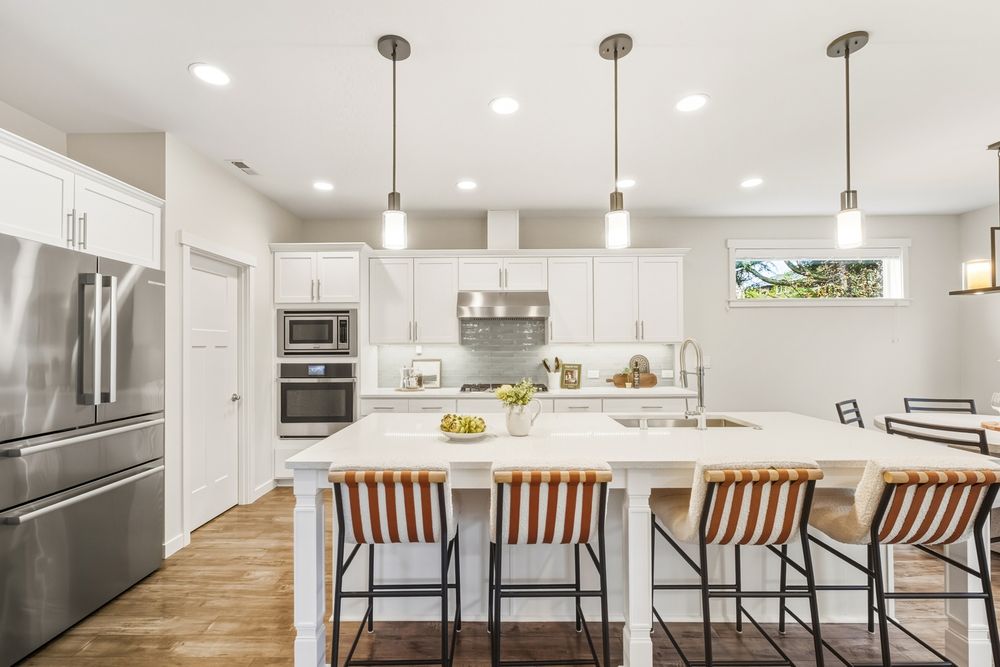 Modern white kitchen with large island, pendant lights, stainless steel appliances, and wood bar stools.