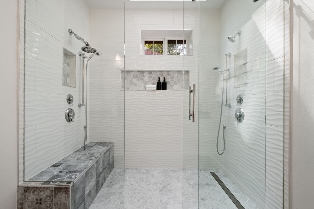 Elegant walk-in shower with white subway tiles, marble bench, dual showerheads, and glass doors in a modern bathroom.