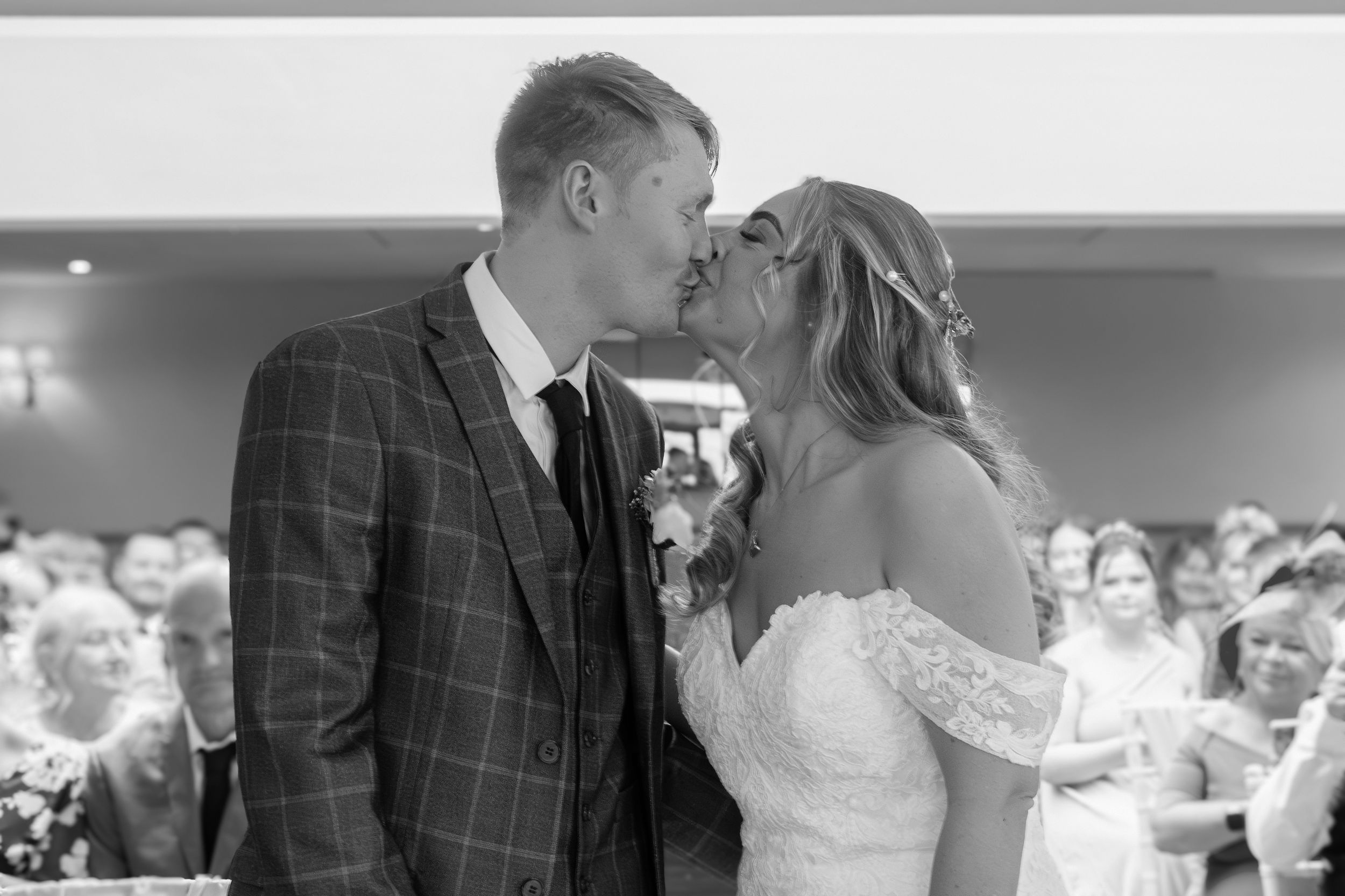 A bride and groom share their first kiss at the altar during their wedding ceremony as guests look on from behind.