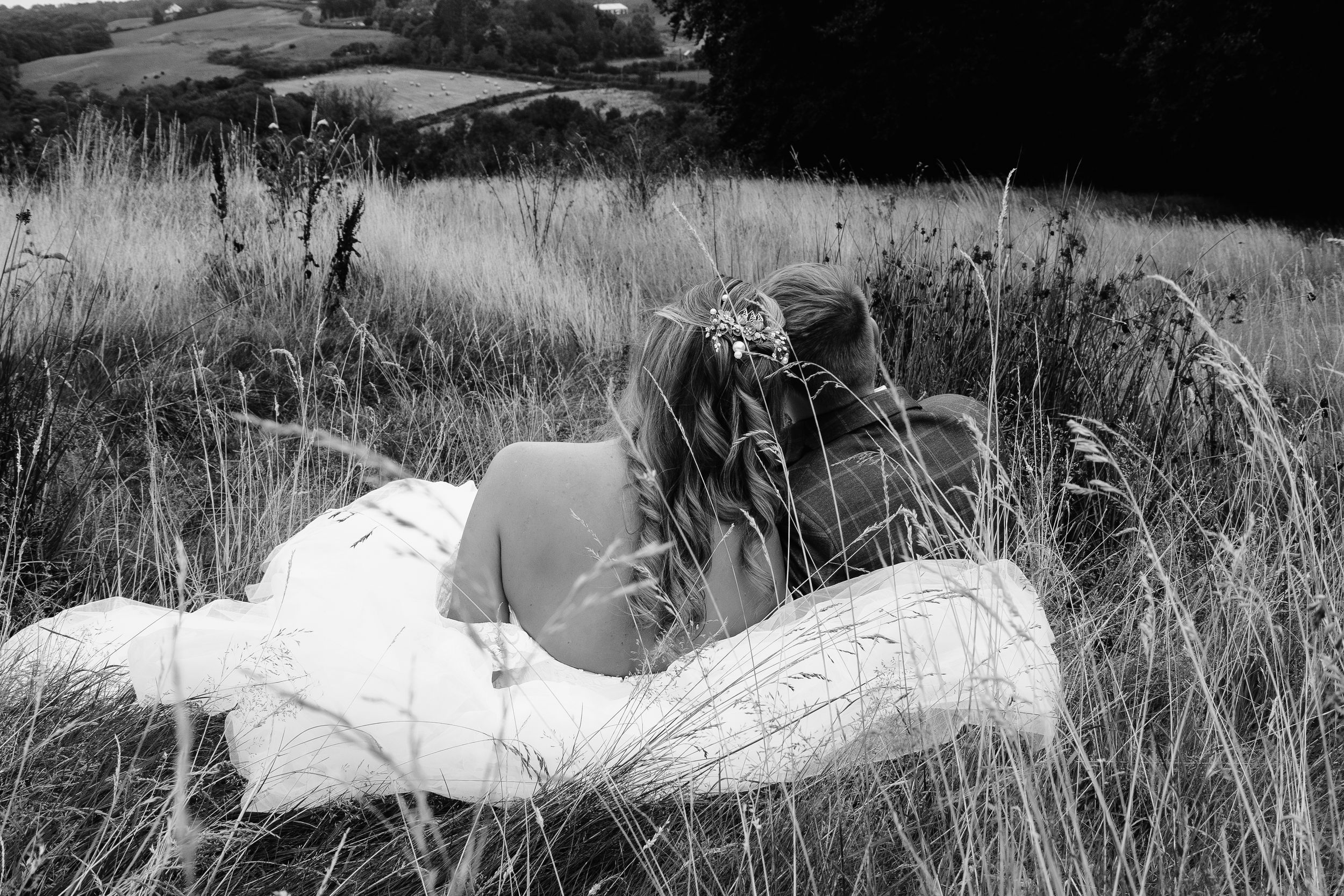 A couple relaxes in tall grass on a sunny afternoon, captured in black and white photography.