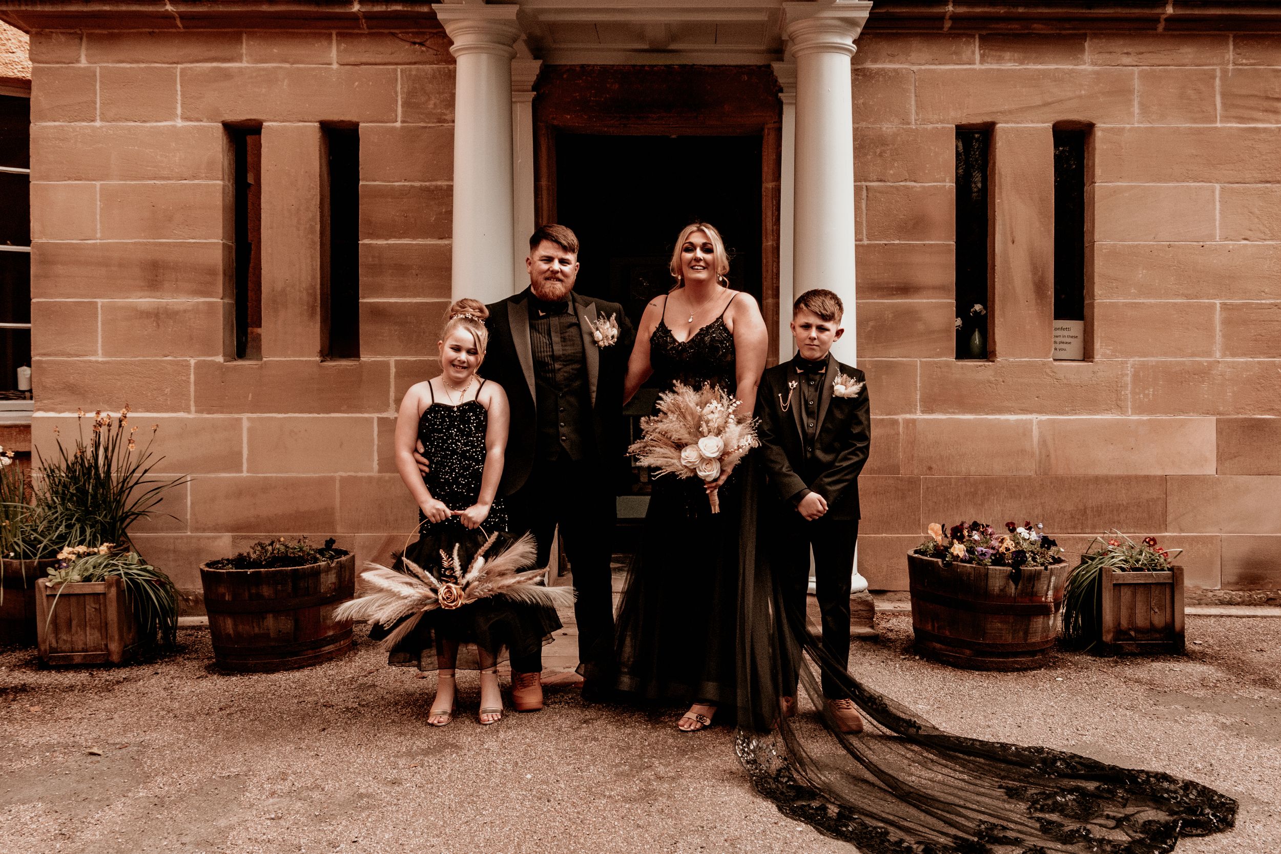 Bride, Groom and their children pose together in front of a stone building with columns.