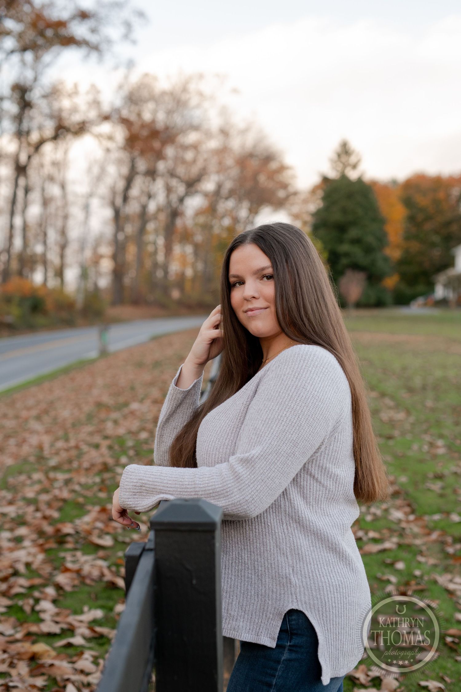 Autumn portrait by wooden fence with long straight hair and light gray sweater.